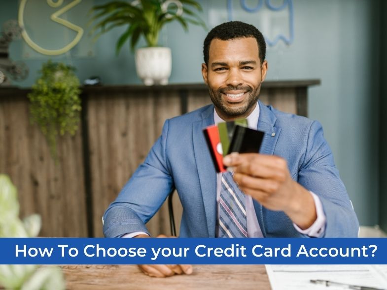 A man is smiling while holding a credit card in front of his desk documents.